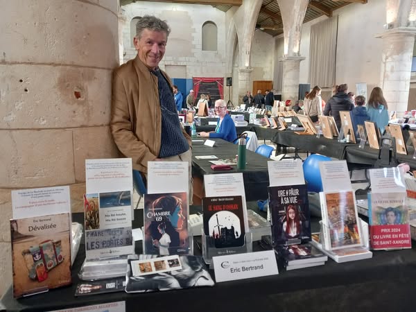 Éric Bertrand devant sa table de livres lors d’un salon